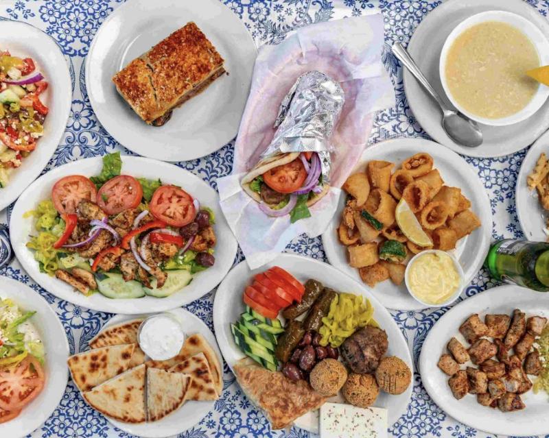 A Nikos spread: gyro, moussaka, souvlaki salad, kalamari, avgolemono, pita and an appetizer plate on a blue-and-white tablecloth